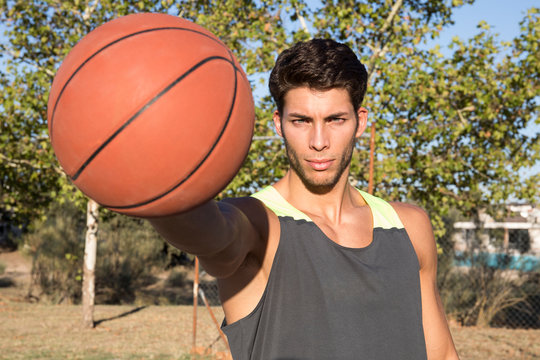 Young serious man in sportswear outstretching hand with basketball, looking at camera