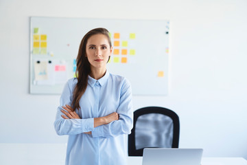 Portrait of confident businesswoman looking at camera with crossed arms in office