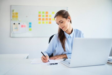 Young businesswoman preparing business documents while working with laptop in office