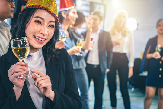 Business Social Gathering Party,New Year's Eve Celebration. Happy Asian Businesswoman In Party Holding Wine Glass With Her Colleagues In The Background.