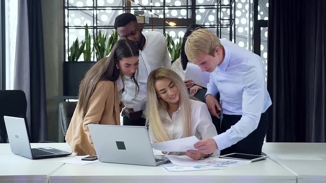 Good-looking purposeful multiracial business group of men and women discussing details of their project at the meeting table in modern office
