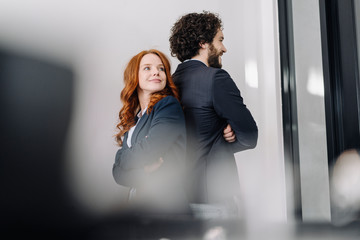 Confident businessman and businesswoman standing back to back in office