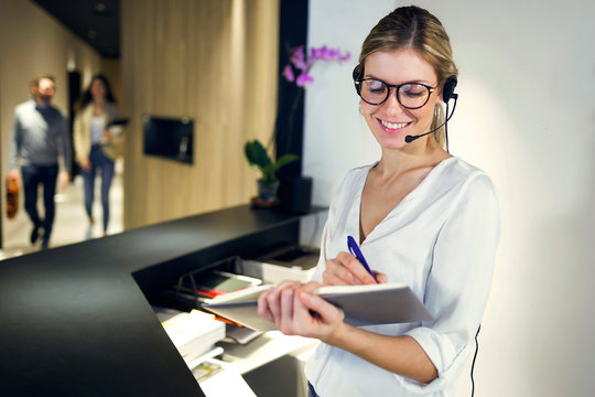 Smiling receptionist talking with headset while taking notes - Powered by Adobe