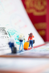 Miniature toys concept studio set up - a lady arrives or departs at an airport and talking to her mobile phone with visa passport stamps as the background.