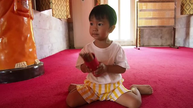 Asian child boy holding and shaking red wooden bamboo stricks equipment box predict fortune teller in buddhist temple.