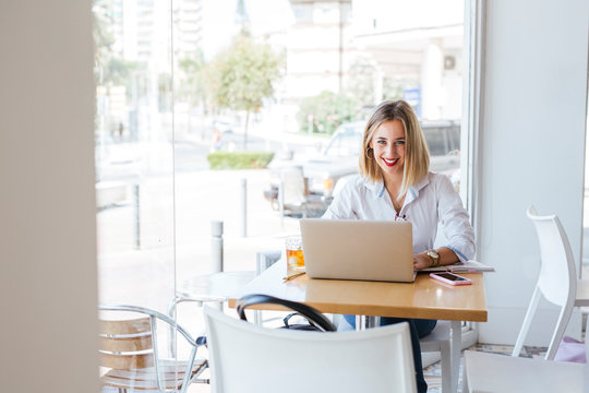 Portrait of smiling young woman with laptop on table in a cafe