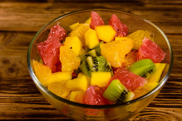 Salad with mango, oranges, grapefruit and kiwi fruits in a glass bowl on wooden table