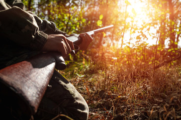 A hunter with a gun in his hands in hunting clothes in the autumn forest close-up. The hunting...