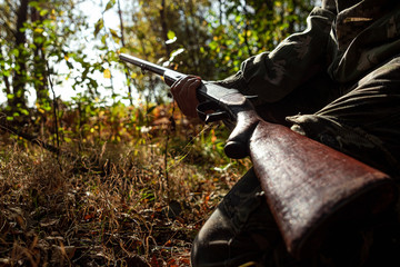 A hunter with a gun in his hands in hunting clothes in the autumn forest close-up. The hunting...
