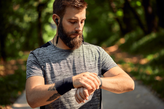 Portrait of sporty man with earphones in forest checking his smartwatch