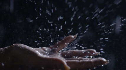Detail mixed race woman's outstretched hand reaches from left to catch falling drops of slow motion rain. Dark, high contrast footage recorded at 120fps. - Powered by Adobe