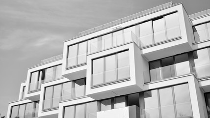  Fragment of a facade of a building with windows and balconies. Modern home with many flats. Black and white.