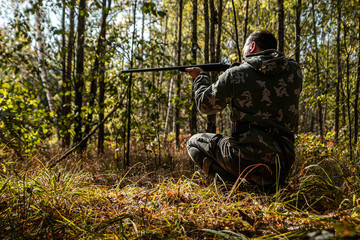 Hunter man in camouflage with a gun during the hunt in search of wild birds or game on the background of the autumn forest. Autumn hunting season. The concept of a hobby, killing.