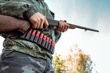 A hunter with a gun in his hands in hunting clothes in the autumn forest close-up. The hunting...