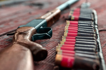 Shotgun and cartridges in patronage are lying on a wooden table top view. The hunting period, the...