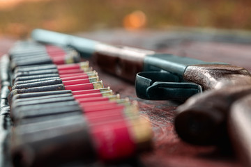 Shotgun and cartridges in patronage are lying on a wooden table top view. The hunting period, the...