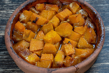 Baked yellow pumpkin with honey, olive oil and spices on a plate on the wooden table. Vegetarian food. Closeup