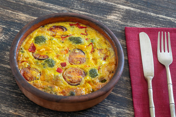 Ceramic bowl with vegetable frittata, simple vegetarian food. Frittata with egg, tomato, pepper, onion, broccoli and cheese on wooden table. Italian egg omelette