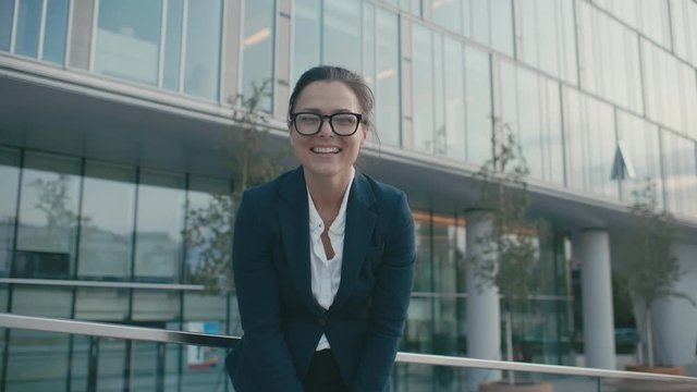 Portrait happy joyful young businesswoman point fingers, taunts at camera. Female laughing enjoying successful lifestyle. Caucasian brunette female outdoors near glass business center facade