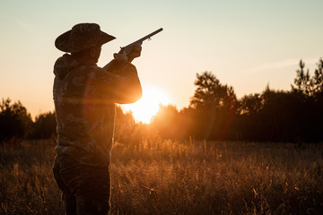 Silhouette of a hunter in a cowboy hat with a gun in his hands on a background of a beautiful...