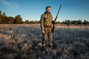 Fototapeta premium Hunter man in camouflage with a gun during the hunt in search of wild birds or game on the background of the autumn forest. Autumn hunting season. The concept of a hobby, killing.