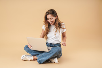 Image of smiling woman using silver laptop while sitting on floor