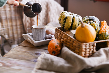 Autumn and winter homemade still life of pumpkins. A girl in a knitted sweater pours freshly brewed coffee into a cup. The concept of home atmosphere and decor. Wooden table biscuit cookies