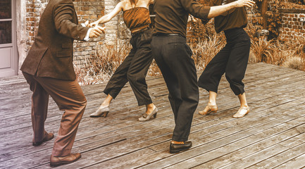 Dance team dancing on the terrace. A view of two pairs dancing in front of a brick building....