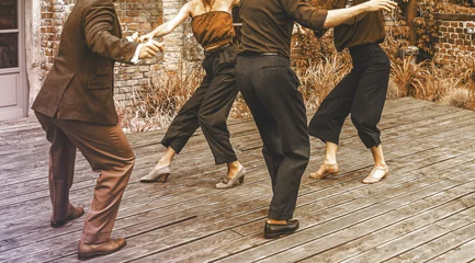 Foto op Plexiglas Dansteam dansen op het terras. Een weergave van twee dansende paren voor een bakstenen gebouw. Silhouetten van jonge mensen die buiten dansen. Swing dansen concept. Bokeh-achtergrond. © Piotr