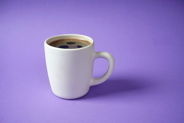 White Cup with black coffee on lilac background. Rest, relaxation, tone.
