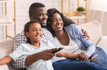 African American Family Of Three Sitting On Sofa Watching Television