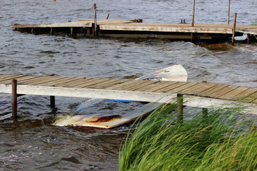Abandoned ittle sunken boat with water under wooden Pier, Hurricane near shore, strond wind,...