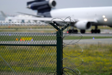 Security fence and starting airplane on takeoff runway at Frankfurt airport in Germany - Stockphoto