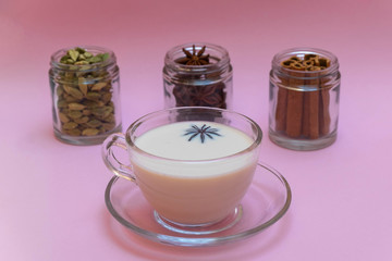 Cup of traditional indian masala tea with cinnamon, anise and cardamom on pink background