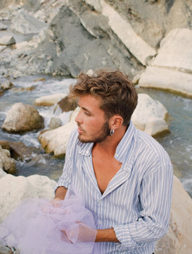 Stylish man holding white tulle by rocky river