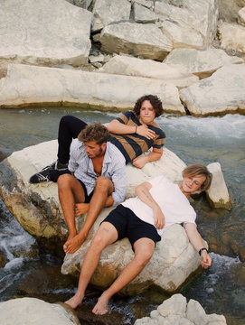 Three young men relaxing on rock by river