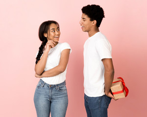 Fototapeta premium Happy guy hiding present from girlfriend, pink background