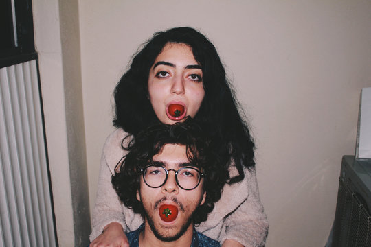 Portrait of two young playful people with tomatoes in mouths