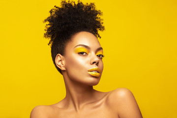 Portrait of Young African American girl model with creative make up posing against yellow background