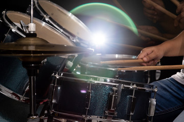 A man is playing drum set in low light background.