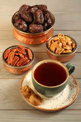 Vegetarian dessert: dried dates, pecans and walnuts in copper bowls, dried figs on a saucer and a cup of black tea on a gray wooden table. Closeup