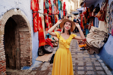 Colorful traveling by Morocco. Young woman in yellow dress walking in  medina of  blue city...
