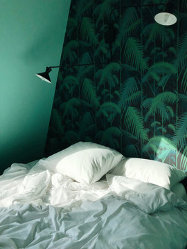 Bed with white sheet and pillow and foliate wallpaper