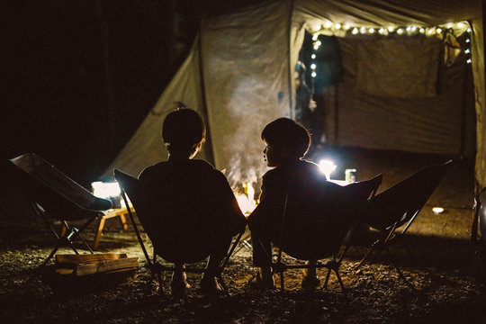 Rear view of siblings sitting near campfire at night