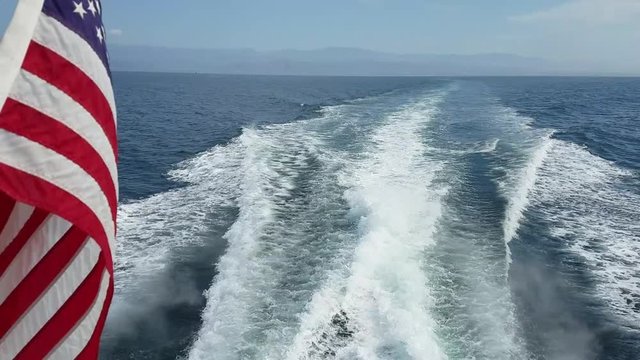 American flag waving and the water wake done by a speeding boat slicing the Pacific ocean near Ventura, California, on a ride to the Channel Islands National Park