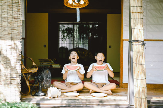 Portrait of siblings eating watermelon slices on patio