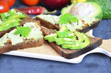 Guacamole with bread and avocado Sandwich with avocado and guacamole. Black cereal bread. Ingredients for making lime, red pepper, tomatoes. Healthy food, diet on a black background