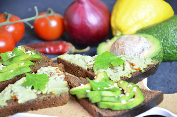 Guacamole with bread and avocado Sandwich with avocado and guacamole. Black cereal bread. Ingredients for making lime, red pepper, tomatoes. Healthy food, diet on a black background