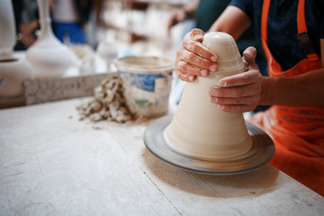 Hands of young potter, was produced on range Hands of a potter skillfully making a pot of white clay.