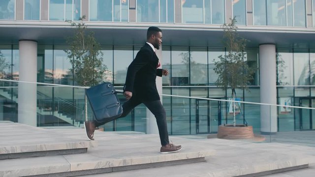 Happy african american business man with briefcase walking after work day in downtown. Handsome young businessman feeling good luck smiling running